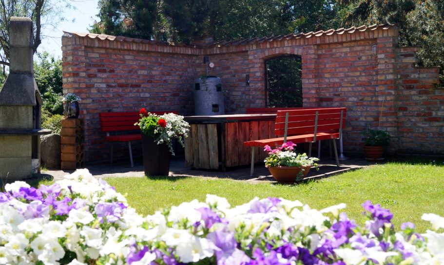 Grillecke Gemütliche Gartenecke mit roten Bänken, Tisch und bunten Blumenbeeten.