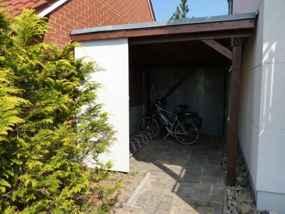 Fahrradgarage Fahrradunterstand neben einem Gebäude, umgeben von Bäumen und gepflastertem Weg.