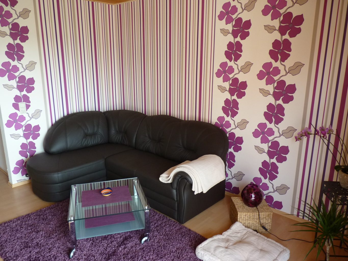 Gemütliche Sitzecke Elegantes Wohnzimmer mit schwarzem Sofa, lila gestreifter Wand und Blumenmotiv.