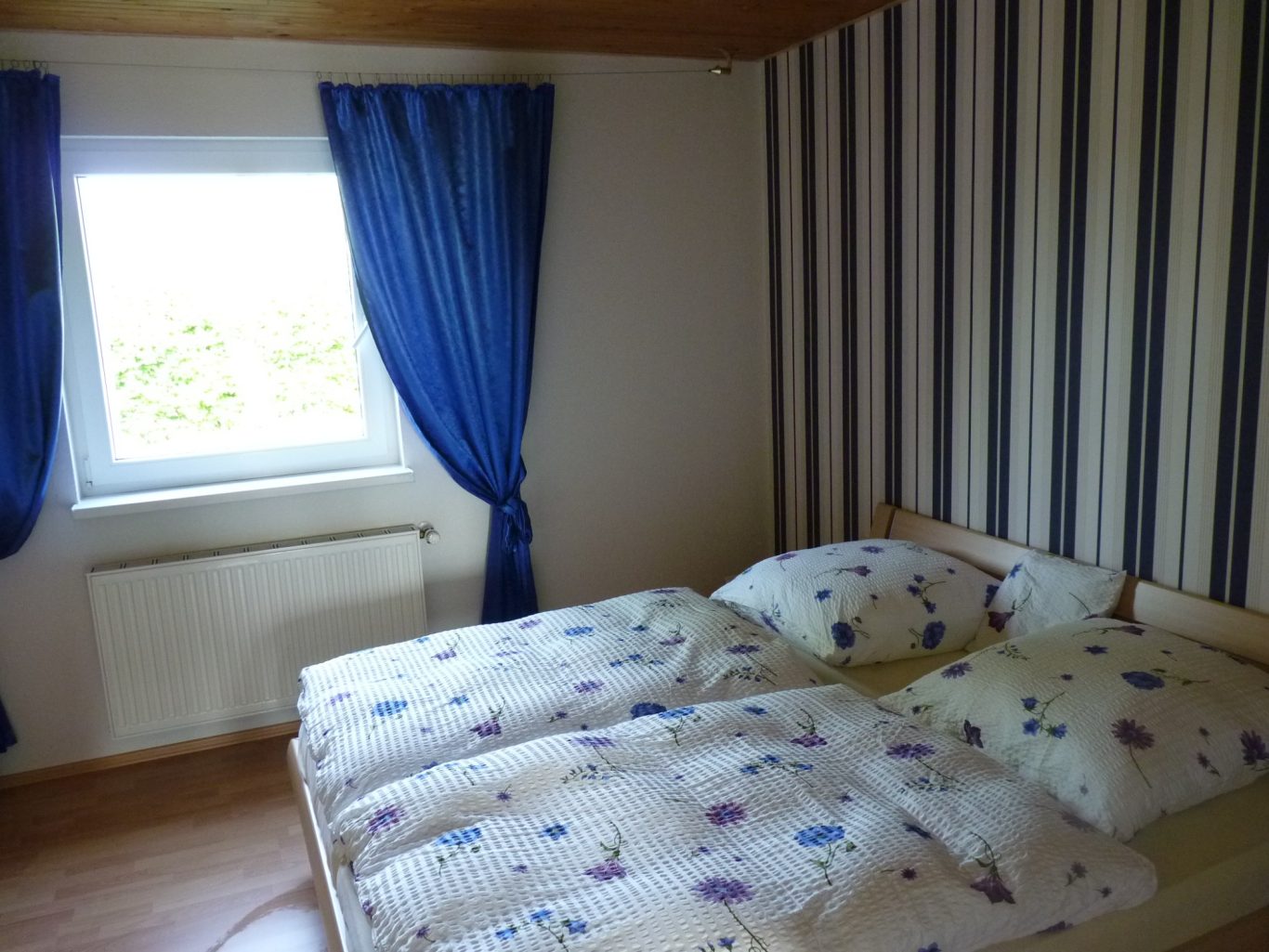 Schlafzimmer Ein Schlafzimmer mit einem Doppelbett, gestreiften Wänden und blauen Vorhängen.