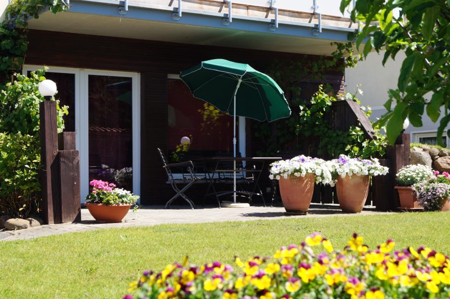 Gartenanlage Blühender Garten mit Terrassenmöbeln und einem grünen Sonnenschirm.