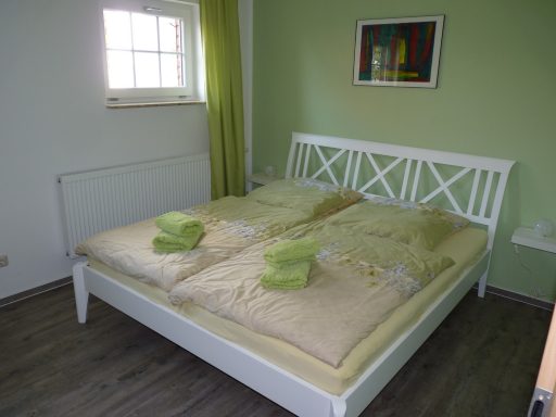 Schlafzimmer Gartenapartment Helle Schlafzimmer mit einem Doppelbett, grünen Handtüchern und einer farbigen Wanddekoration.